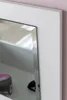 A close-up view of a white framed mirror with a beveled edge, reflecting a shelf with a cosmetic jar and a black object. Produktbild-Vorschau