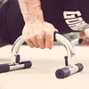 A close-up shot of a person's hand gripping a chrome push-up bar with black foam grips, performing a push-up. Náhľad obrázku produktu