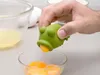 A hand is using a green frog-shaped egg separator to extract an egg yolk from a bowl of egg yolks. Produktbild-Vorschau