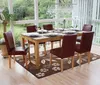 A dining room set with a wooden table and six red-brown chairs, set with plates and glasses, in a sunlit room with large windows overlooking a garden. Náhled obrázku produktu