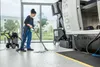 A woman is cleaning a workshop floor with a vacuum cleaner next to a large industrial machine. Voir les images du produit