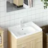 A close-up view of a white ceramic sink with a wooden vanity underneath, set against a white tiled wall. Podgląd zdjęcia produktu