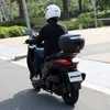 A person riding a black scooter on a paved road. Anteprima dell’immagine prodotto