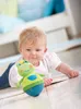 A baby is lying on the floor playing with a frog toy. Produktbild-Vorschau