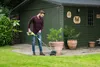 A man is using a Ryobi trimmer in a garden next to a green shed. Podgląd zdjęcia produktu