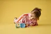 A young girl is lying on a yellow surface, playing with small Lego cubes. Anteprima dell’immagine prodotto