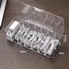 A clear plastic organizer box filled with coiled cables and power adapters, placed on a wooden desk. Produktbild-Vorschau