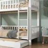 A white wooden bunk bed with a pull-out trundle bed is shown in a room with a light green wall and wooden floor. Anteprima dell’immagine prodotto