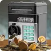 A close-up shot of a black and silver electronic piggy bank with a keypad and a slot for coins, surrounded by scattered coins. Náhled obrázku produktu