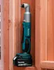 A cordless angle impact driver is shown mounted on a wooden wall. Náhled obrázku produktu