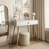 A white console table with a drawer and wooden legs, a round stool, and a large arched mirror in a room with artwork on the wall and curtains. Produktbild-Vorschau