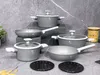 A set of grey cookware with white handles is displayed on a grey, textured surface, with a jar of pasta in the background. Podgląd zdjęcia produktu