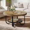 A round coffee table with a wooden top and black metal legs is placed on a rug in a living room setting. A vase of flowers and a book are on the table. Náhľad obrázku produktu