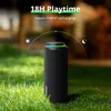 A black outdoor speaker sits on green grass with a blurred background of trees and foliage. The speaker has a colorful LED light ring around the top. Náhľad obrázku produktu