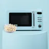 A light blue retro-style microwave oven is shown on a light blue pedestal, with a bowl of popcorn in front of it. Podgląd zdjęcia produktu