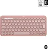 A rose-colored Logitech Pebble Keys 2 K380s keyboard is shown from a front-facing, slightly elevated angle against a white background. The keyboard features round keys and a compact design. In the top right corner, there are two small certification badges. Produktbild-Vorschau