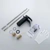A black faucet and its accessories are laid out on a white and light gray background. Produktbild-Vorschau
