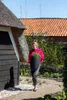 A woman is carrying a potted plant in a garden next to a thatched-roof building. Náhľad obrázku produktu