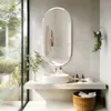A modern bathroom with a large oval mirror above a sink and shelf. Voir les images du produit
