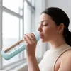 A woman drinks from a water bottle in front of a window. Náhľad obrázku produktu