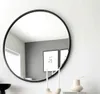 A round mirror with a black frame is displayed on a wall, reflecting a room with artwork and a window. Anteprima dell’immagine prodotto