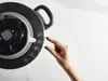 A hand is shown pressing a button on the control panel of a black pressure cooker. Voir les images du produit
