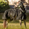 A horse wearing a black and gold turnout rug with a neck cover, standing in a grassy field with a building in the background. Voir les images du produit
