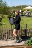 A woman is carrying a potted plant in a garden. Náhľad obrázku produktu
