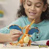 A young girl smiling while holding a toy Charizard Pokemon figure made of building blocks. Voir les images du produit