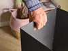 A person's hand is holding a black metal basket, with a pink woven basket and magazines in the background. Anteprima dell’immagine prodotto
