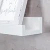 A close-up view of a white shelf with a picture frame on it, against a textured gray wall. Produktbild-Vorschau