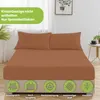 A bed with a brown fitted sheet and two pillows, set in a bedroom with a plant and a side table. Produktbild-Vorschau