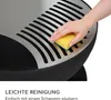 A hand is cleaning a metal grate on a black outdoor fire pit with a yellow sponge. Produktbild-Vorschau
