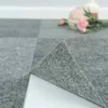A close-up of grey carpet tiles, with one tile lifted to show the adhesive backing. Produktbild-Vorschau