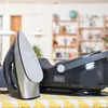 A black steam iron and its base are displayed on a yellow and white striped tablecloth in a well-lit room. Produktbild-Vorschau
