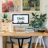 A well-lit home office desk setup with a computer, lamp, plants, and artwork. Produktbild-Vorschau