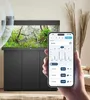 A hand holding a smartphone displaying an app interface, with a modern aquarium in the background. Voir les images du produit