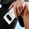 A person's hand holding a transparent phone case with a black frame, with water droplets on the hand and phone case, resting on a person's knee. Produktbild-Vorschau