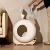 A person is holding a bag of cat litter next to a white, circular cat litter box. Náhled obrázku produktu