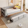 A light gray upholstered daybed with a pull-out trundle bed is shown in a room with a rug and a robot vacuum cleaner. Produktbild-Vorschau