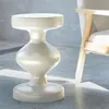 A cream-colored metal side table is placed next to a chair in a room with a concrete floor and wall. Anteprima dell’immagine prodotto