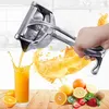A hand is using a manual juicer to squeeze juice into a glass, with various fruits scattered on a wooden surface. Náhľad obrázku produktu
