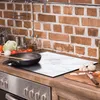A kitchen counter with a stove, cooking utensils, and ingredients. Anteprima dell’immagine prodotto