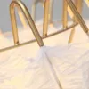 A close-up view of a gold-colored metal structure with white feathers attached. Podgląd zdjęcia produktu