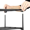 A person's hands are assembling a black metal shoe rack. Náhled obrázku produktu