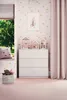 A child's bedroom with a white dresser, decorative house-shaped shelves, a unicorn picture, and a pink curtain.