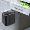 A black hanging trash can with a white lid is attached to the side of a kitchen cabinet, next to an open drawer containing cleaning supplies. Anteprima dell’immagine prodotto