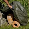 A person is covering terracotta pots with a green tarp. Produktbild-Vorschau
