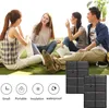 Four young people are sitting on a grassy area, talking and interacting. Two folded black cushions are placed in the foreground. Podgląd zdjęcia produktu