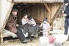 A family is gathered in a rustic wooden shelter, with sheepskins on the seating and floor. Produktbild-Vorschau